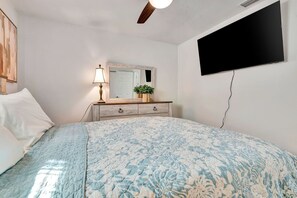 A bedroom with a bed, a dresser, a mirror, a wall-mounted TV, and a ceiling fan. - Favour warminera spring-Charming 3-bedroom house with AC in tranquil North Port (North Port)