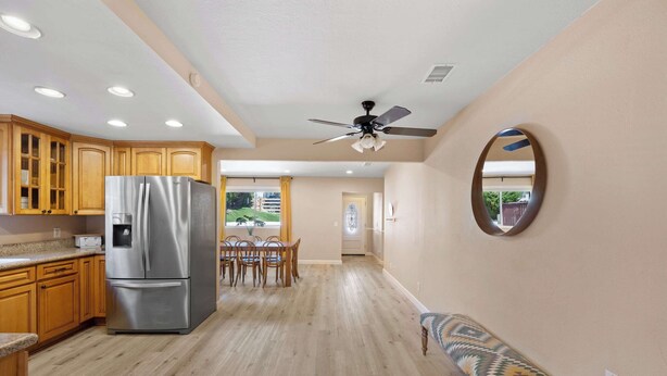Una cocina amplia con armarios de madera, un refrigerador de acero inoxidable, un comedor con mesa y sillas, y un ventilador de techo.