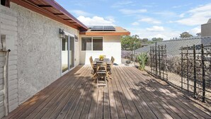 Una terraza de madera con una mesa y sillas, un panel solar en el techo y un jardín vallado.