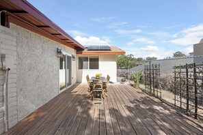 A wooden deck with a table and chairs, a solar panel on the roof, and a fenced garden area. - Spacious and Serene North Park Home (San Diego)