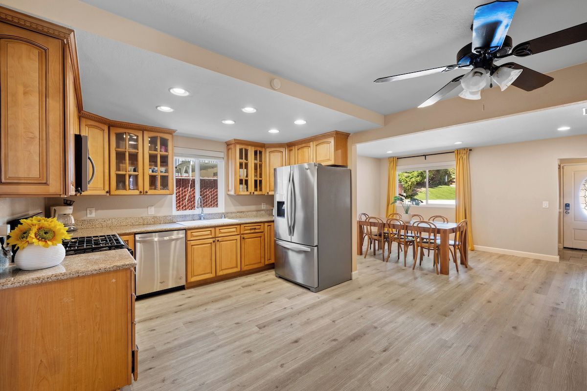 A kitchen with wooden cabinets, a stainless steel refrigerator, and a dining area with wooden chairs.