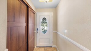 Un pasillo con una puerta de madera, una puerta de cristal con diseño decorativo y una lámpara en el techo.