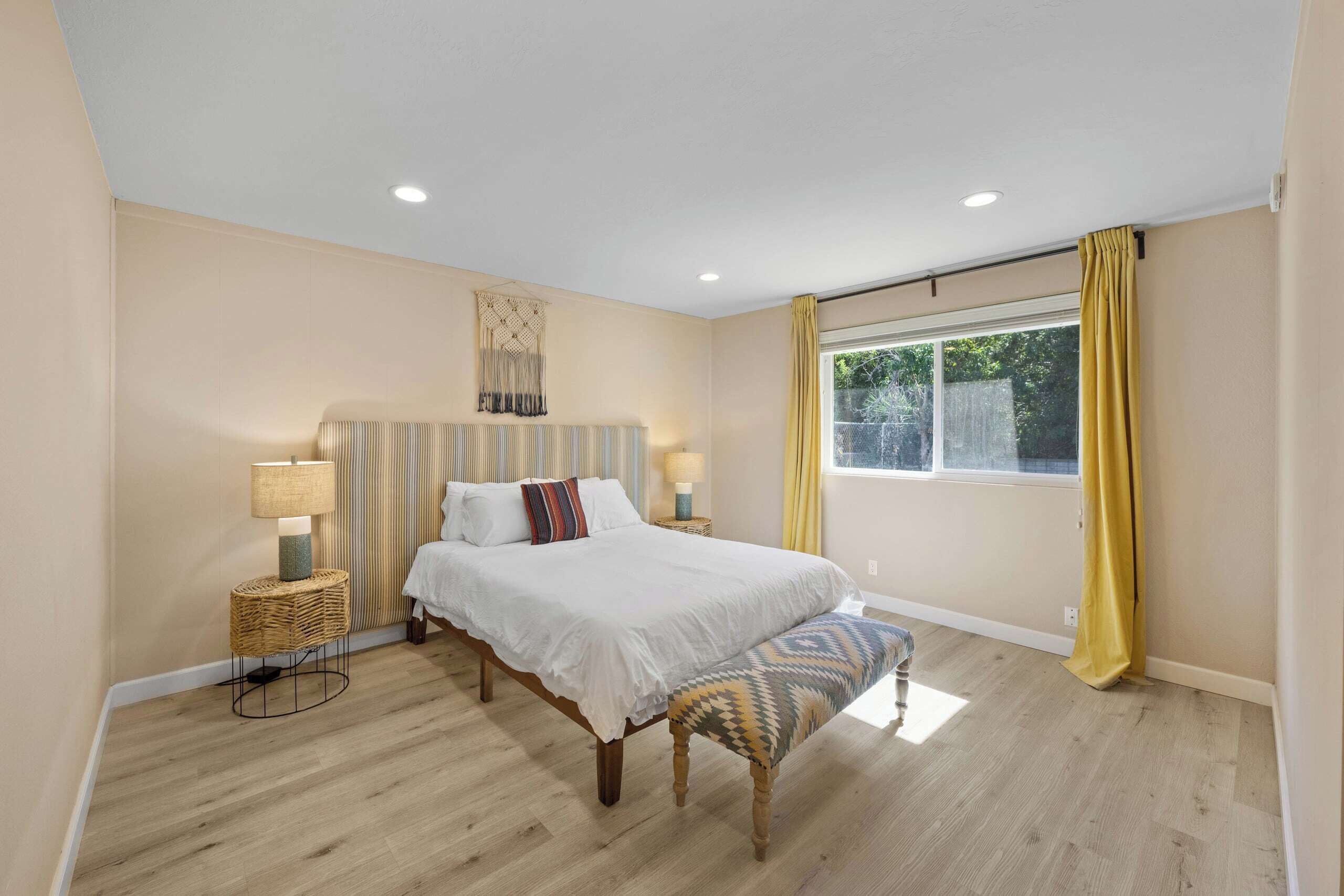 A bedroom with a bed, bedside tables, a window with curtains, and a wall-mounted decorative piece.
