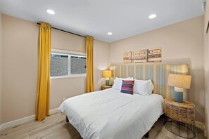 A bedroom with a bed, two bedside lamps, a window with curtains, and a wall with three framed pictures. - Spacious and Serene North Park Home (San Diego)