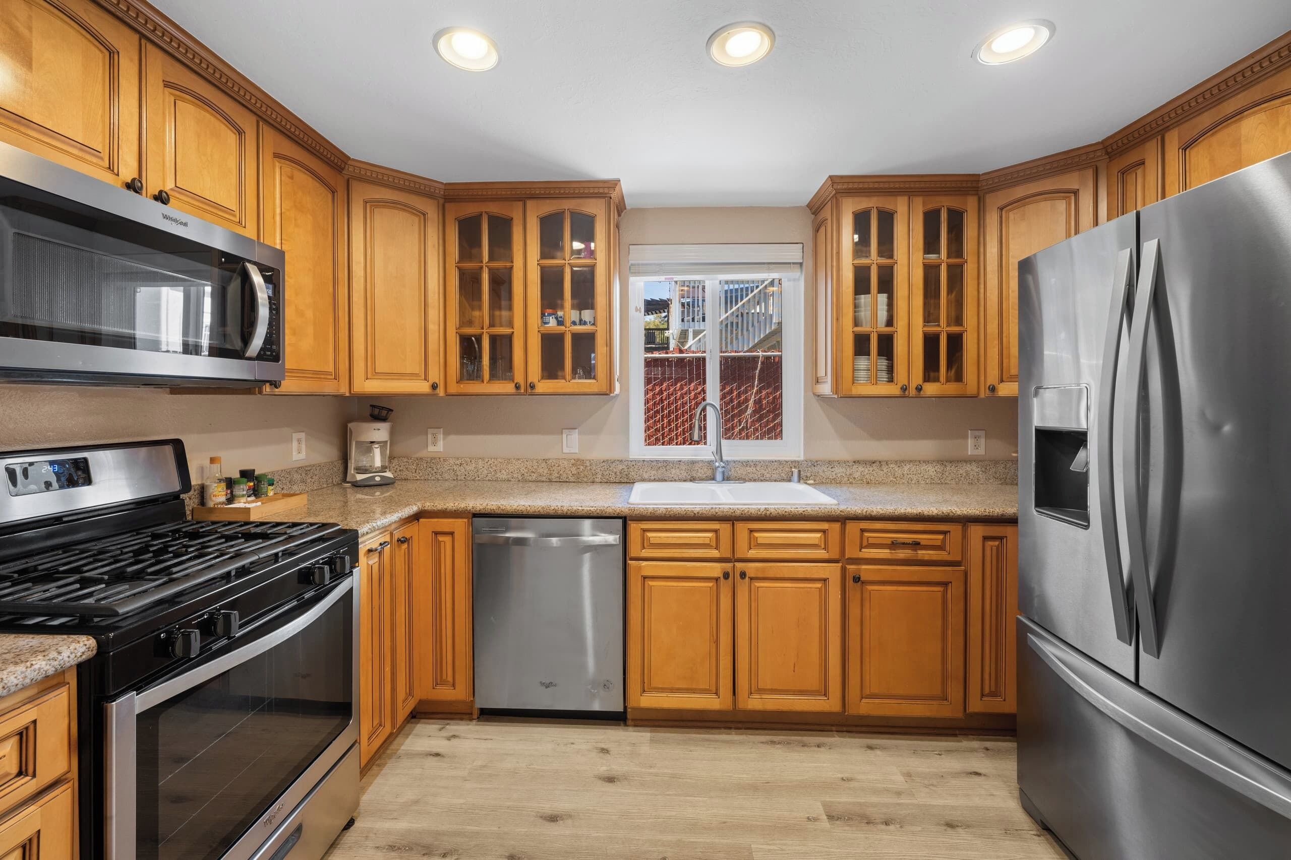 Una cocina moderna con gabinetes de madera, electrodomésticos de acero inoxidable y un ventanal con vista a una cerca roja.