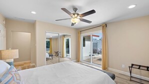 Un dormitorio con cama, ventilador de techo, puerta corrediza al balcón y vistas al exterior.