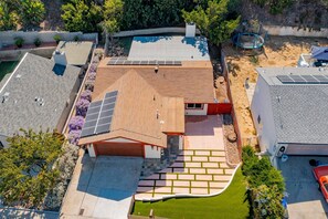 A residential property with a sloped roof, solar panels, a swimming pool, and a well-maintained lawn. - Spacious and Serene North Park Home (San Diego)