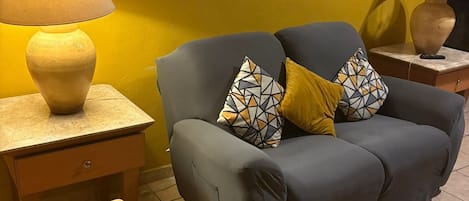 Un salon avec un canapé, deux lampes, un miroir et un tableau encadré accroché au mur.