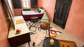 A room with a bed, a small table with a cup, a decorative rug, and a door. - Charming 5-Bedroom Mini Riad with Patio, Gym and Inspiring Workspace (Marrakech)