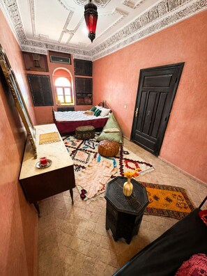 Una habitació amb un llit, una taula petita amb una tassa, un estenedor decoratiu i una porta.