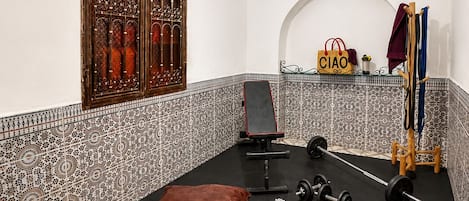 A gym with a black rubber floor, weightlifting equipment, a bench, and a decorative wall with a window and patterned tiles.