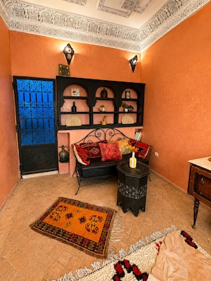 A room with a sofa, a small table, a decorative shelf, and a patterned rug. - Charming 5-Bedroom Mini Riad with Patio, Gym and Inspiring Workspace (Marrakech)