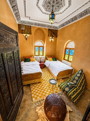 Una habitación con dos camas, un tapete estampado, un reposapiés de cuero y apliques decorativos.