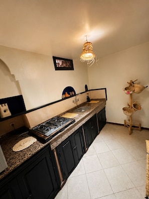 A kitchen with a gas stove, a sink, and a hanging light fixture. - Charming 5-Bedroom Mini Riad with Patio, Gym and Inspiring Workspace (Marrakech)