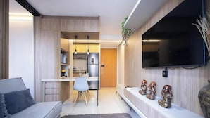 Un salon moderne avec un canapé, un coin repas comprenant une table et des chaises, un espace cuisine avec un réfrigérateur et des placards, et un téléviseur fixé au mur.