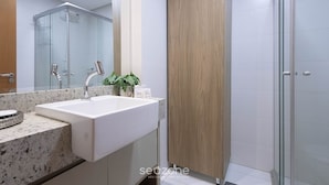 Une salle de bain moderne avec un lavabo blanc, une douche en verre et une porte en bois.
