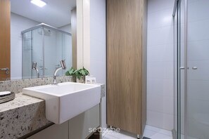 A modern bathroom with a white sink, a glass shower enclosure, and a wooden door. - Studio in Condo. w/ Pool & Balcony Lhg0506 (Goiânia)