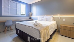 Une chambre à coucher comprenant un lit, une table de chevet, une chaise, une fenêtre avec des stores et un luminaire fixé au mur.