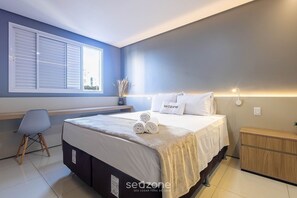 A bedroom with a bed, a bedside table, a chair, a window with blinds, and a wall-mounted light. - Studio in Condo. w/ Pool & Balcony Lhg0506 (Goiânia)