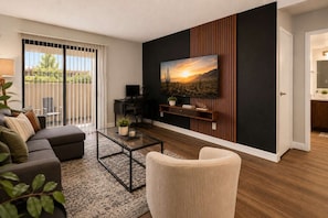 A modern living room with a sofa, coffee table, and a TV mounted on a wall with a desert landscape painting. - Sol Haven Retreat Near ASU, Pool, & Gym | Tempe (Tempe)
