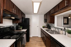 A modern kitchen with dark wood cabinets, a black refrigerator, a stove, and a microwave. - Sol Haven Retreat Near ASU, Pool, & Gym | Tempe (Tempe)