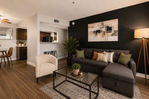 A modern living room with a dark-colored sofa, a glass coffee table, and a dining area with a white table and chairs. - Sol Haven Retreat Near ASU, Pool, & Gym | Tempe (Tempe)