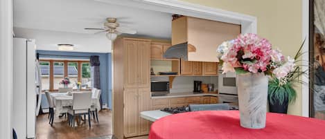 A dining area with a red tablecloth, a vase with flowers, and a kitchen in the background.