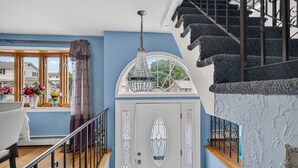 Una scala con ringhiera decorativa, una porta bianca con un vetro e un lampadario a sospensione.