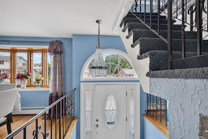 Una escalera con barandilla decorativa, una puerta blanca con panel de vidrio y un candelabro colgante.