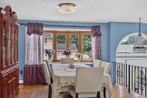 A dining area with a table set for four, a wooden cabinet, and a view of the outside through large windows. - Superb 6-bedroom house with AC in Historic Salem (Salem)