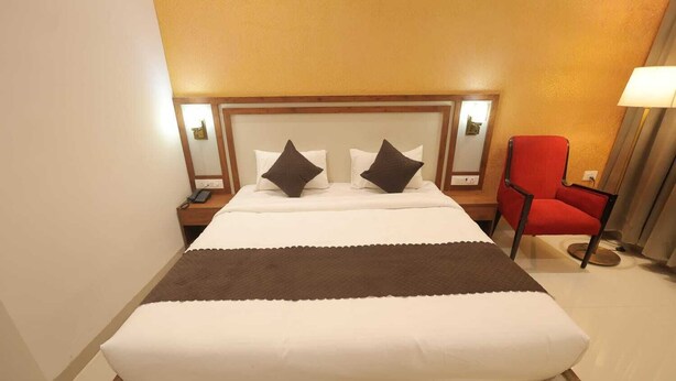 Hotellihuone, jossa on suuri sänky, kaksi yöpöytää, punainen tuoli ja lamppu.