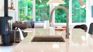 A modern kitchen with a stainless steel faucet, a built-in sink, and a large window offering a view of greenery. - Slo | Luxury, Spa & 2 Saunas Memphremagog lake (Stanstead)