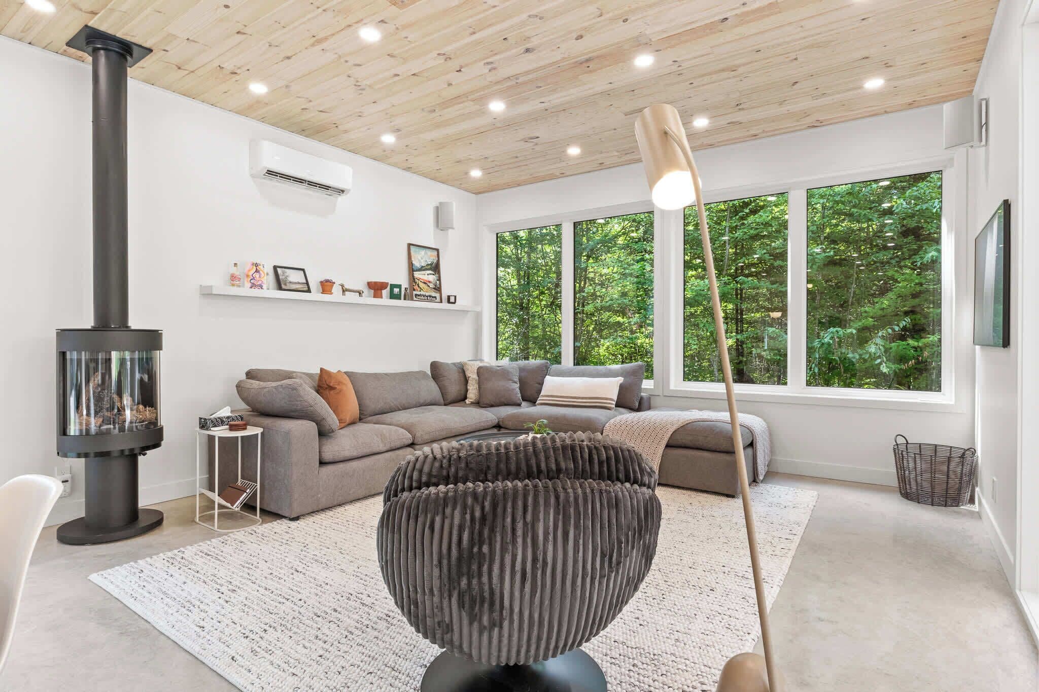 Una sala de estar moderna con un sofá modular, una chimenea de vidrio y ventanas amplias con vista al bosque.