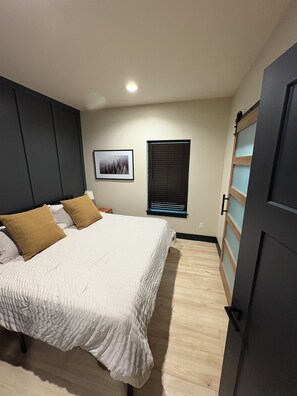 A bedroom with a bed, a window with blinds, a framed picture on the wall, and a wardrobe. - The Bellaire Bunkhouse (Bellaire)
