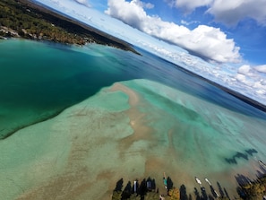 An aerial view of a coastal area with clear water, a sandy beach, and a forested hill. - The Bellaire Bunkhouse (Bellaire)