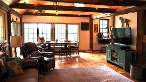 A cozy living room with a fireplace, a television, and a dining area with a table and chairs. - Cozy cabin w/modern amenities in charming Gilford. Pet & family friendly. (Gilford)