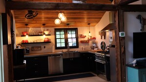A kitchen with wooden beams, a stainless steel dishwasher, an oven, and a window with a view of greenery. - Cozy cabin w/modern amenities in charming Gilford. Pet & family friendly. (Gilford)
