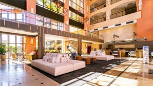 A spacious lobby with a high ceiling, a central seating area with sofas, a reception desk, and a staircase leading to upper floors. - Studio With Balcony in a Cond. With Pool Jbv0432 (Florianópolis)