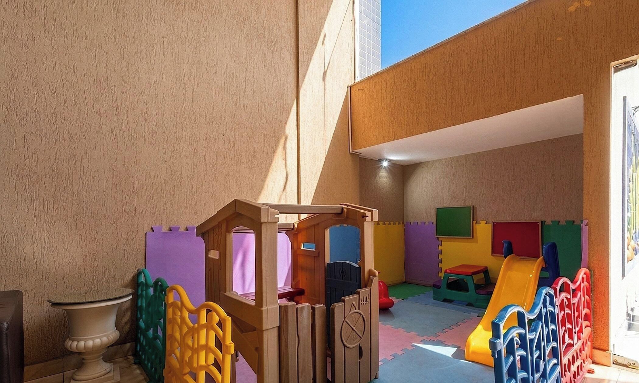 Un área de juegos infantiles con una casita de madera, bloques de espuma de colores y un tobogán.