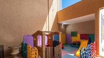 Un área de juegos infantiles con una casita de madera, bloques de espuma de colores y un tobogán.