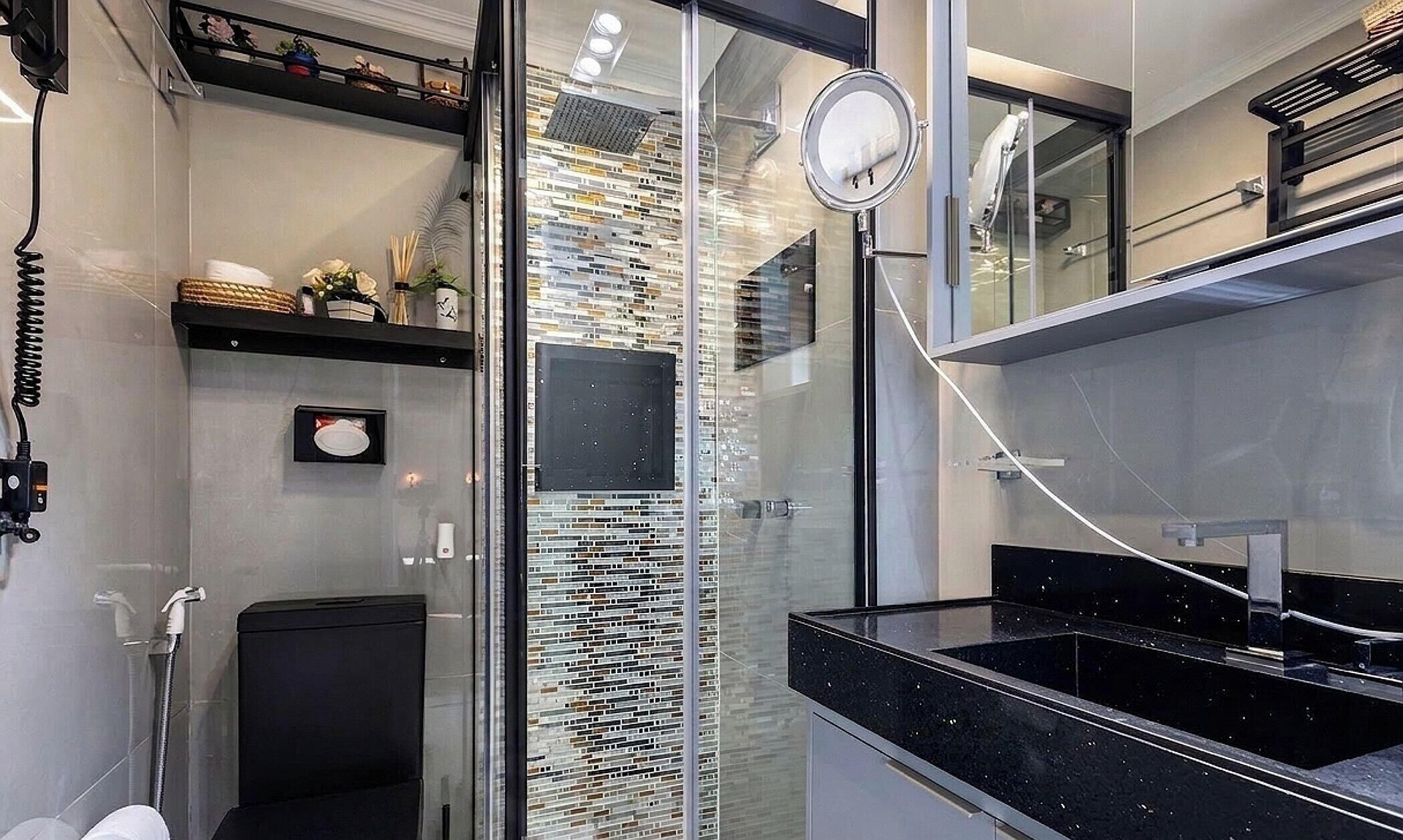 Um banheiro moderno com box de vidro, bancada preta e painel de azulejos.