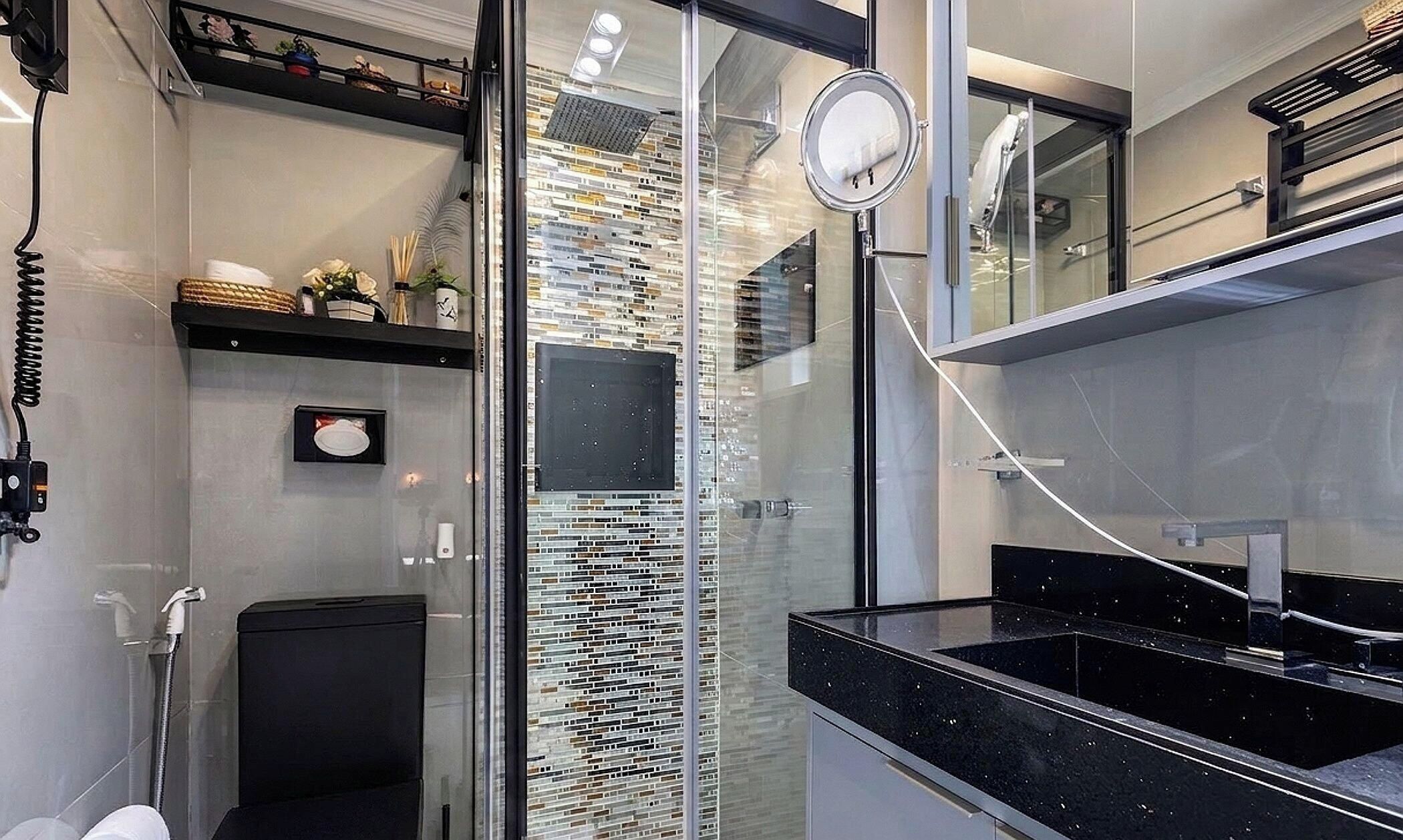 Un baño moderno con cabina de ducha de vidrio, encimera negra y pared decorativa con diseño de mosaico.