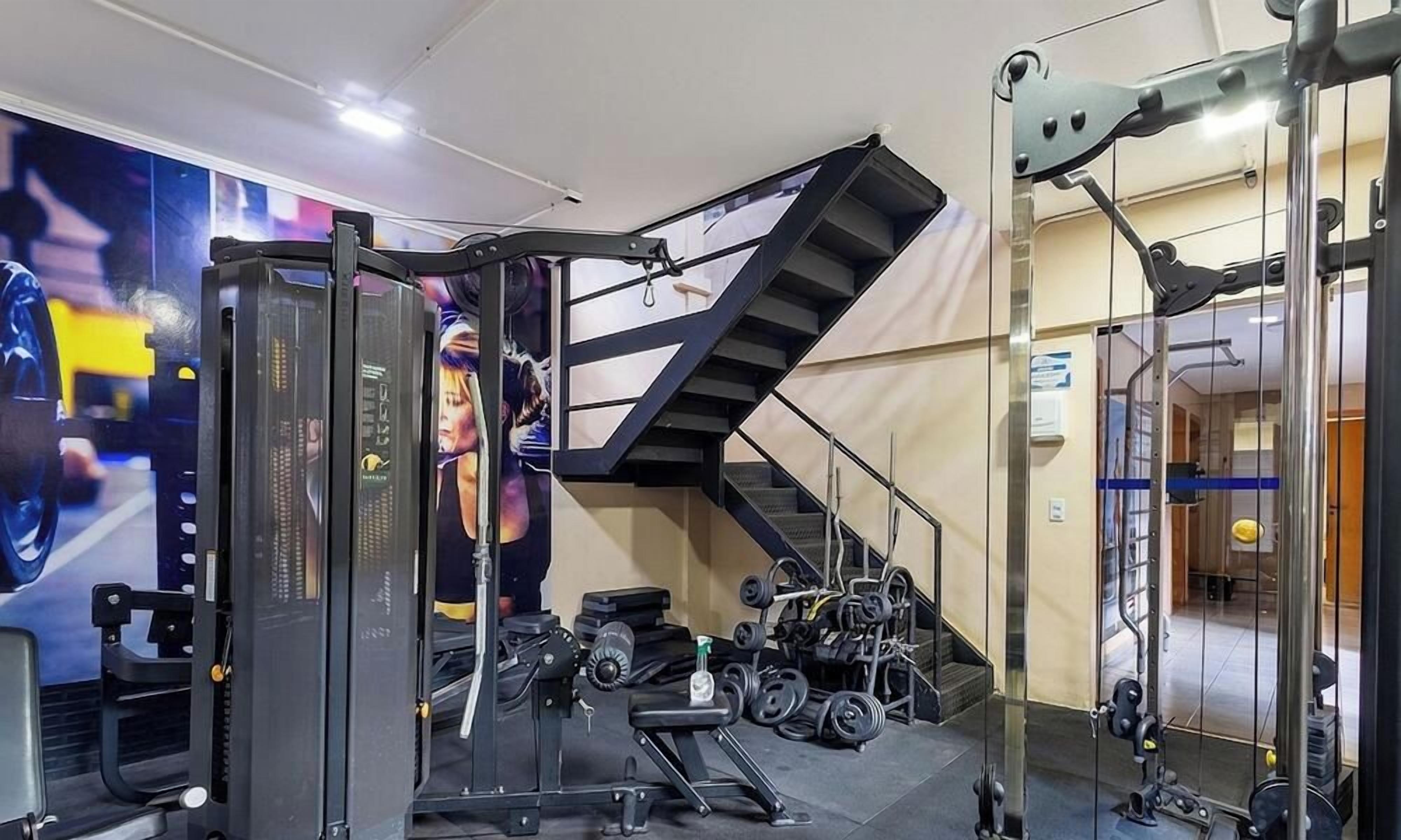 A gym with a variety of exercise equipment, including a squat rack, benches, and dumbbells.