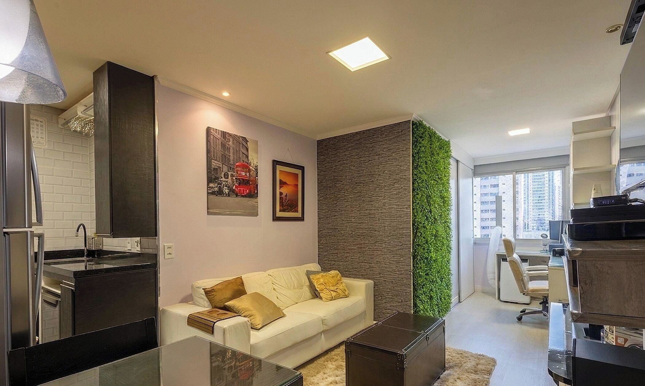 Una sala de estar moderna con sofá, una mesa de centro y una zona de cocina con refrigerador y lavaplatos.