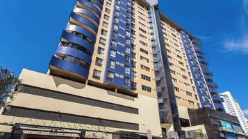 Un edificio de varios pisos con balcones, una zona comercial en la planta baja y un cielo despejado.