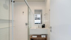 Ein modernes Badezimmer mit Duschkabine aus Glas, einem weißen Waschbecken und einem Spiegel darüber.