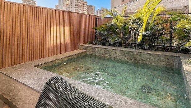 Ein Dachpool mit Holzzaun, Steinrand und tropischer Bepflanzung.
