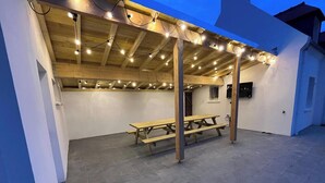 Een overdekt terras buiten met een houten bank en lichtslinger.