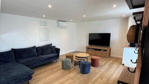 Een moderne woonkamer met een donkergrijze bank, een flatscreen televisie en een houten salontafel.