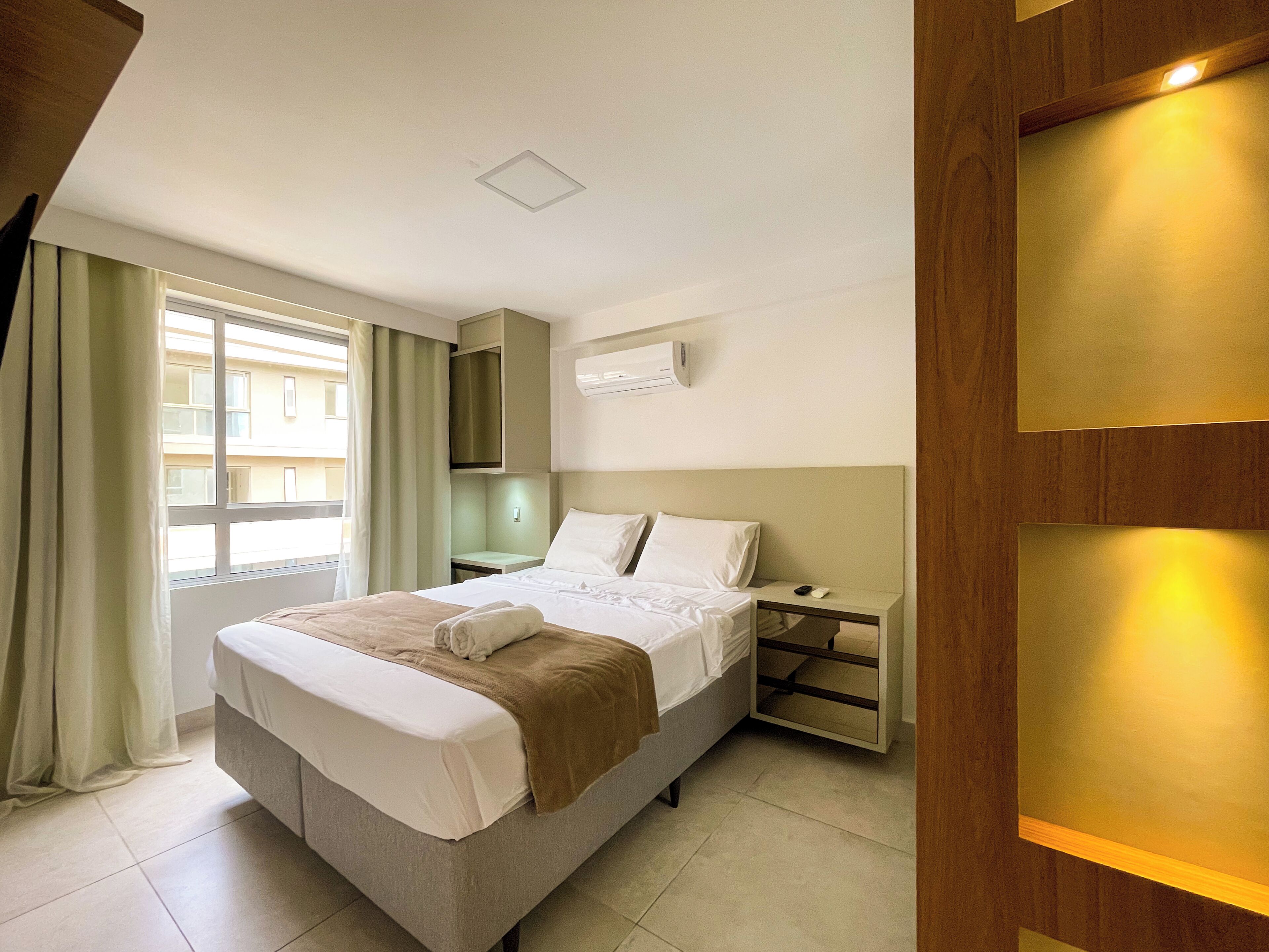 A hotel room with a bed, bedside table, and a window with curtains.